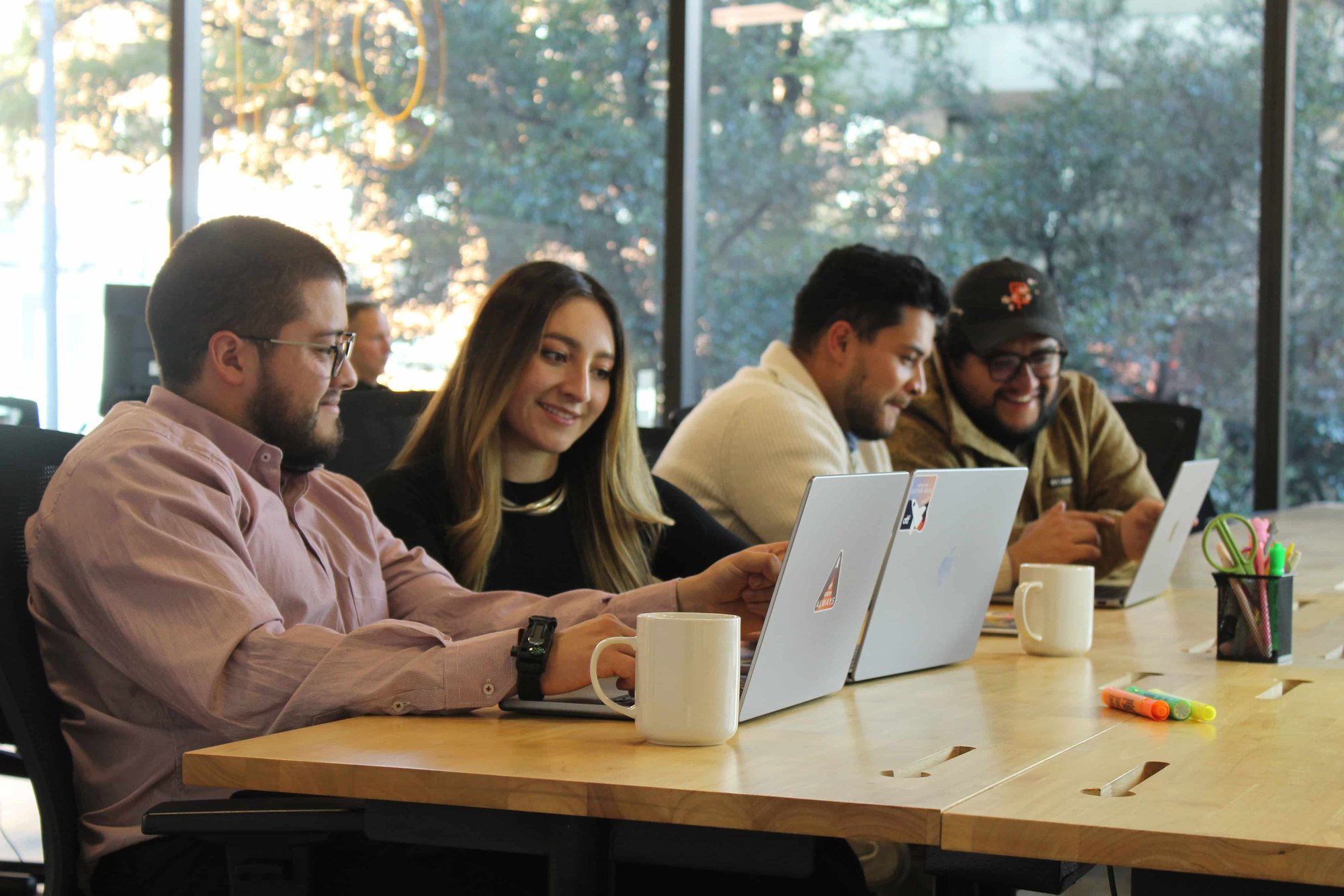 Diverse OTF team members collaborating around conference table with laptops in bright office